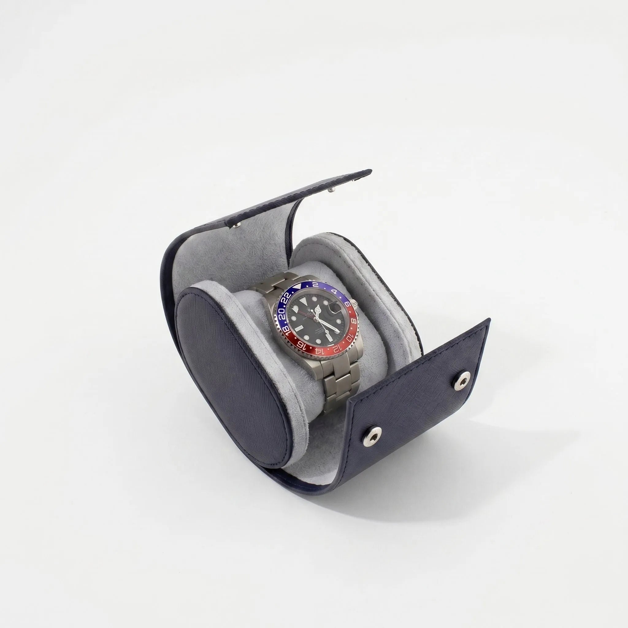 Close-up of navy blue saffiano leather watch roll with soft lighting and subtle shadow on a white background.