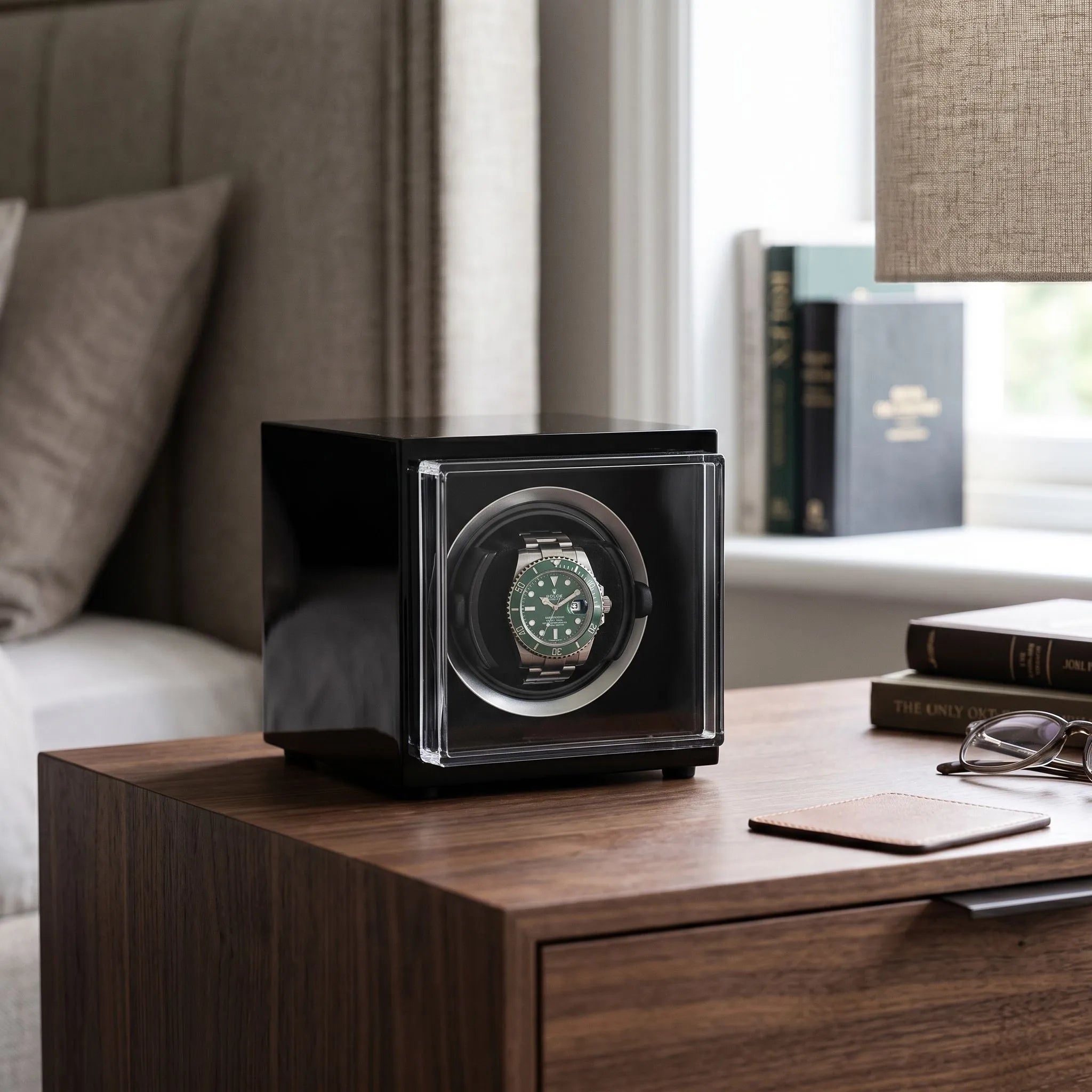 Aevitas single watch winder in high gloss black with a green automatic watch, displayed on a wooden bedside table.